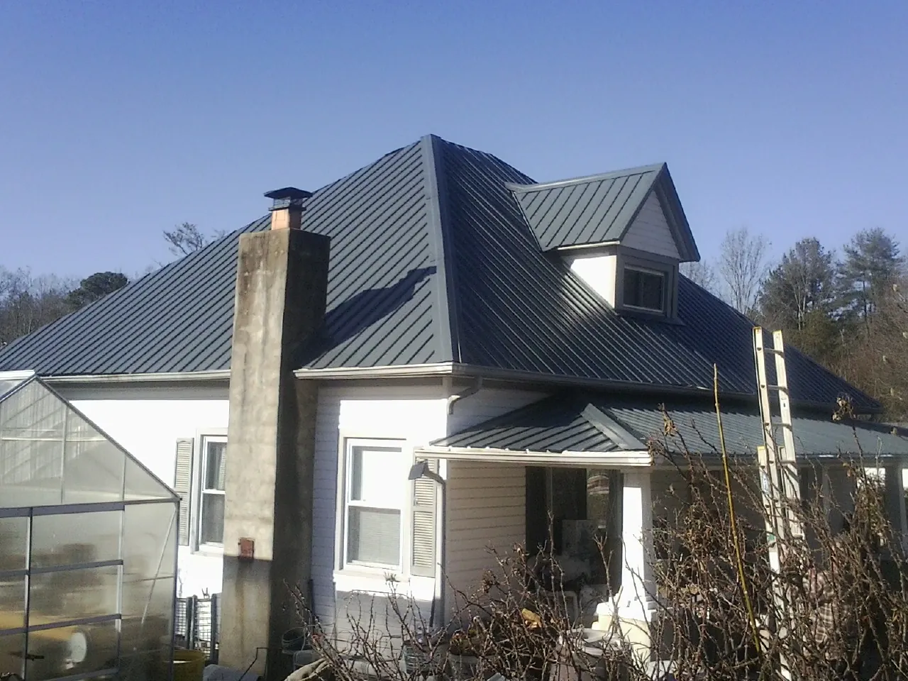 Dark blue standing seam metal roof on a white farmhouse with dormer — Slate & Tile Roof Repair by Roofing Brothers in Huddleston