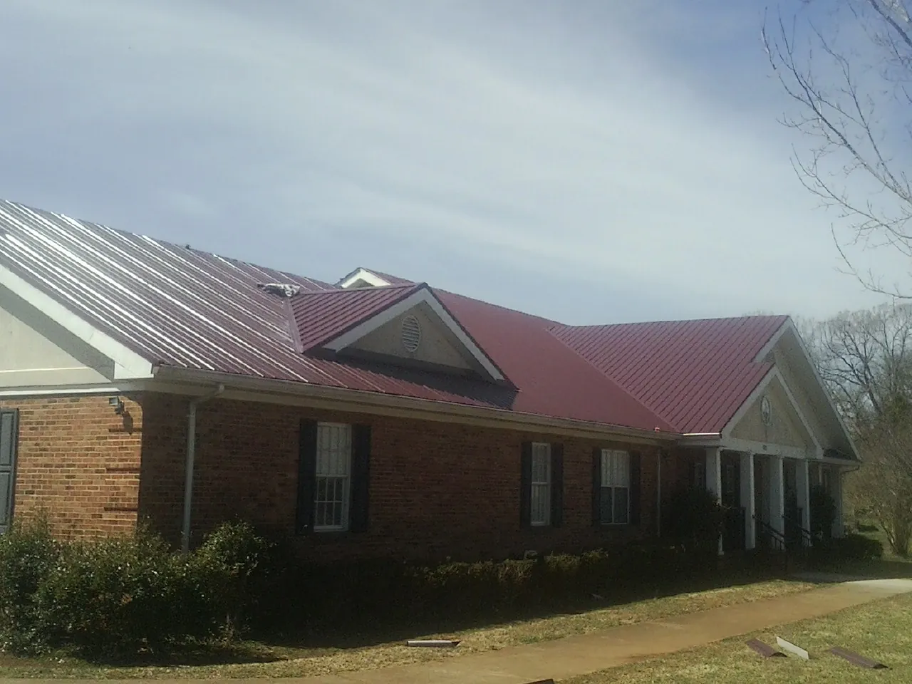 Red metal roof with gabled entries on a long brick building, from a Hail Damage Roof Repair job in Huddleston