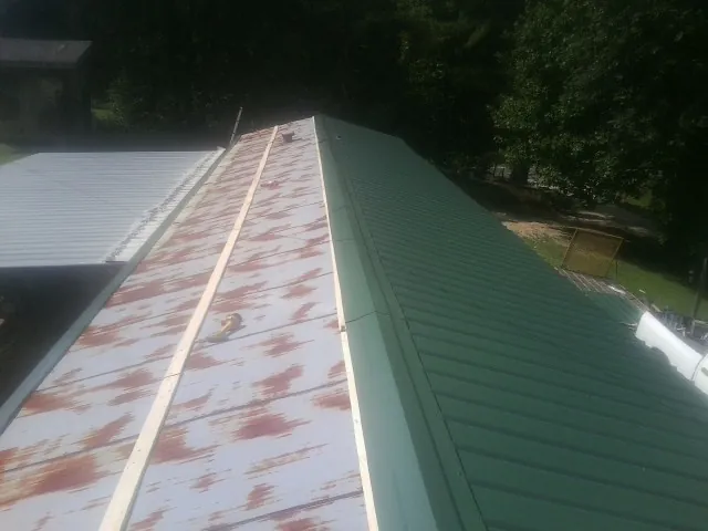 Old rusted panels beside newly installed green metal roofing — Wind Damage Roof Repair by Roofing Brothers in Huddleston