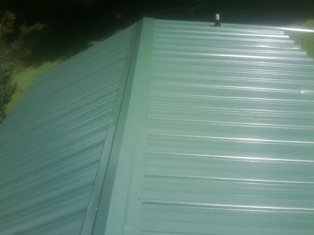 New green metal panels meeting at the ridge of a roof — Flat Roof Repair work by our crew in Huddleston