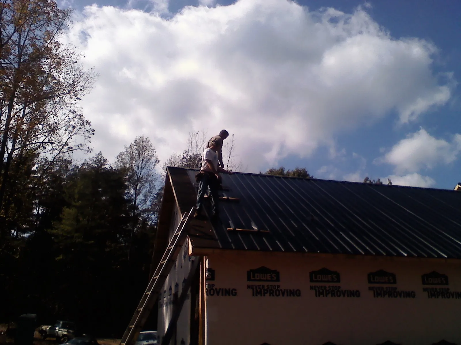 Roofer fastening dark metal panels high against a cloudy sky, from a Roof Inspection job in Huddleston
