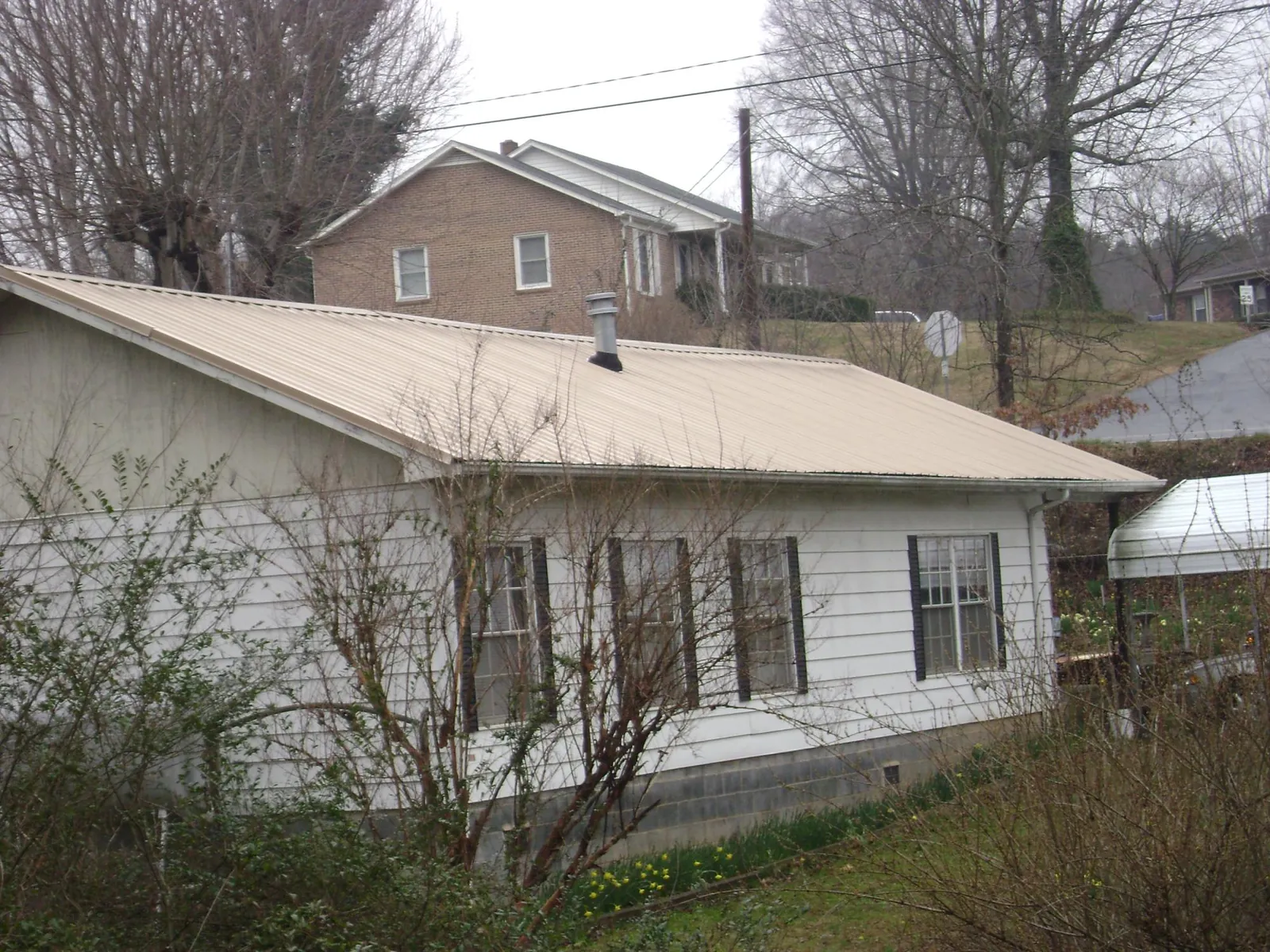 Tan metal roof on a white sided house set into a hillside — Commercial Roofing by Roofing Brothers in Huddleston