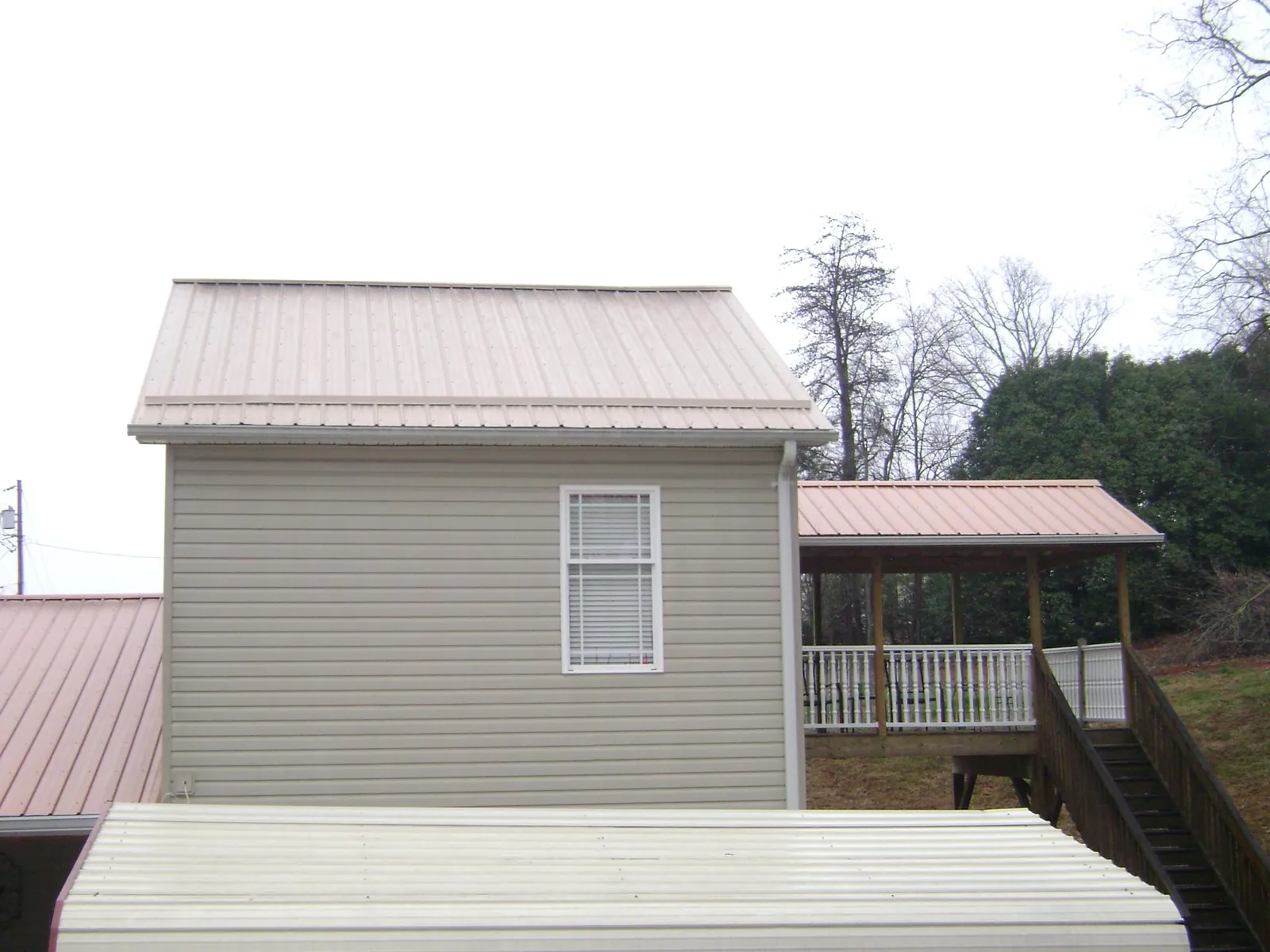 Tan metal roofs on a two story addition and attached porch, from a Roof Replacement job in Huddleston